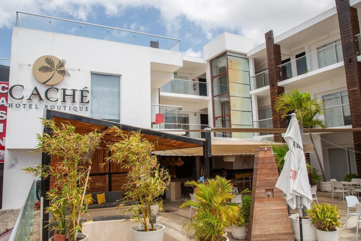 Exterior of the white, modern Caché Hotel Boutique with a patio area, potted plants, and a partial view of the building.