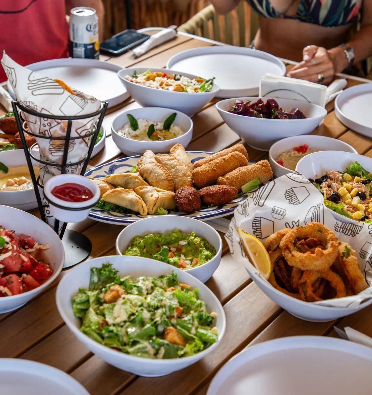 A table filled with various bowls of salads, appetizers, and snacks, surrounded by empty plates for a shared meal.