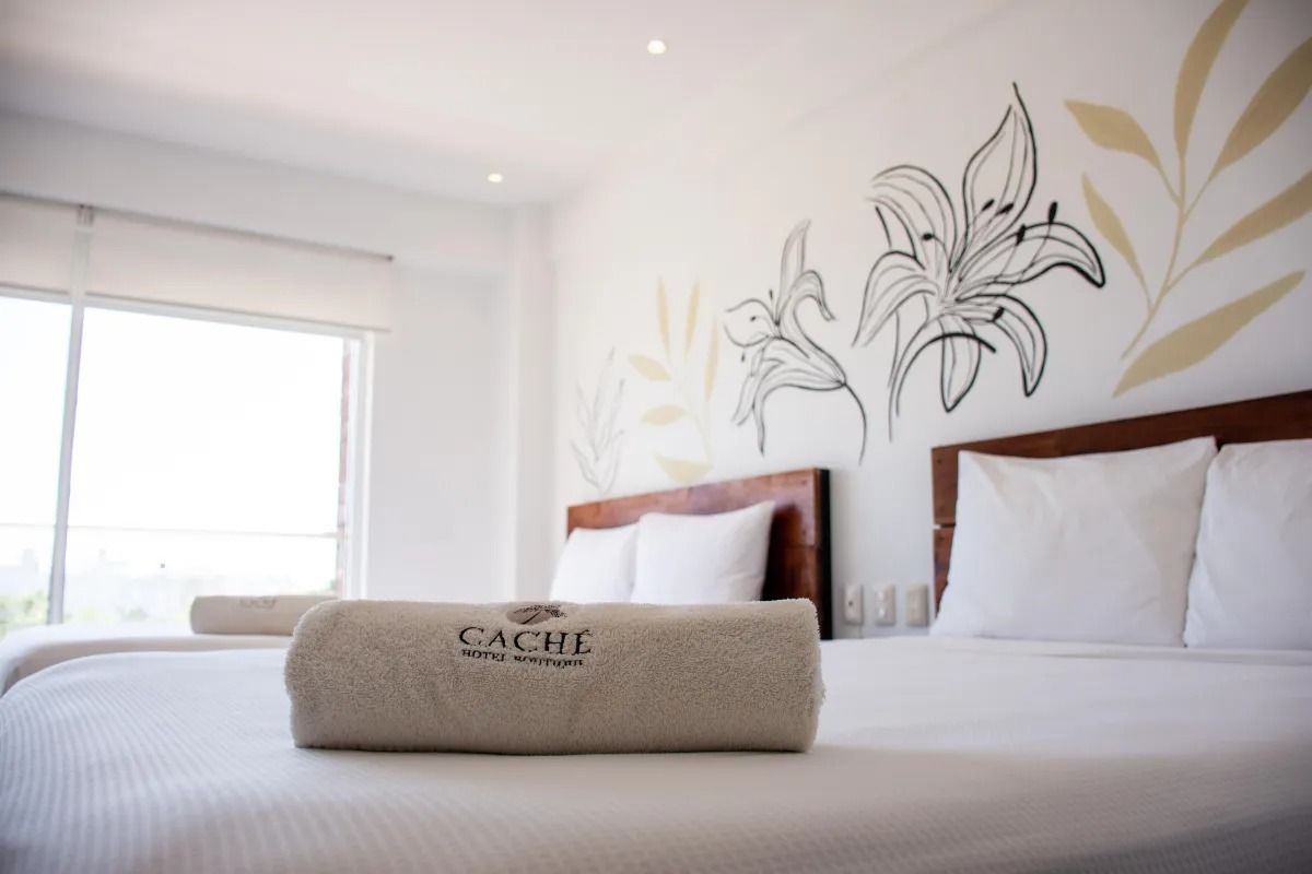A hotel room with two beds featuring white bedding, wood headboards, and black floral wall art.
