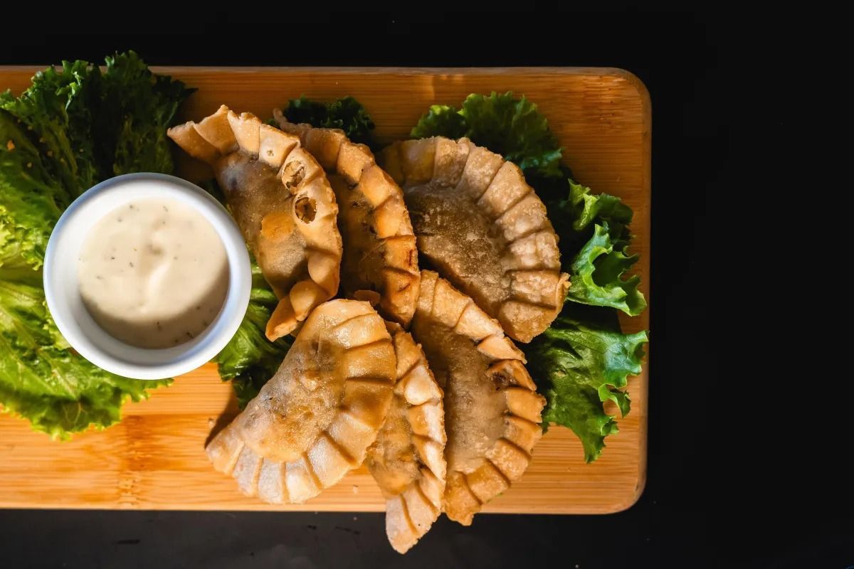 Fried empanadas arranged on a wooden board with fresh lettuce and a small white bowl of dipping sauce.