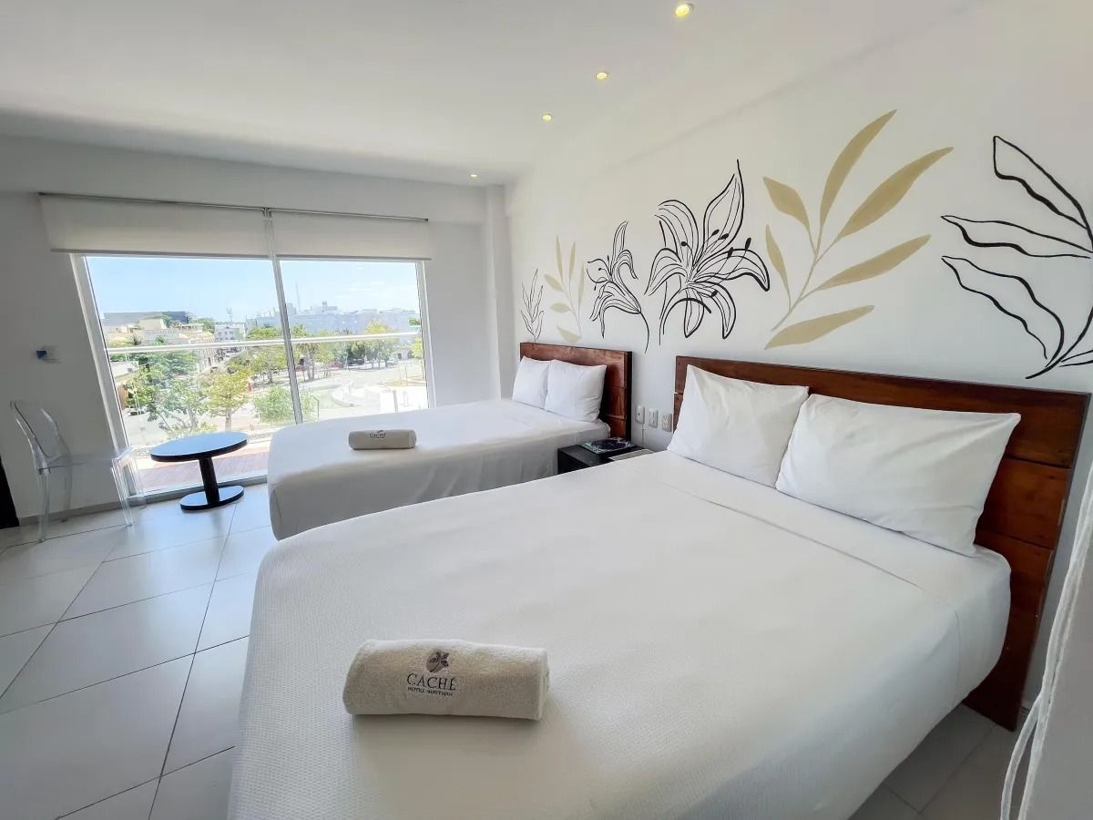 Hotel room with two white beds, a wooden headboard featuring floral artwork, and large windows with a view.