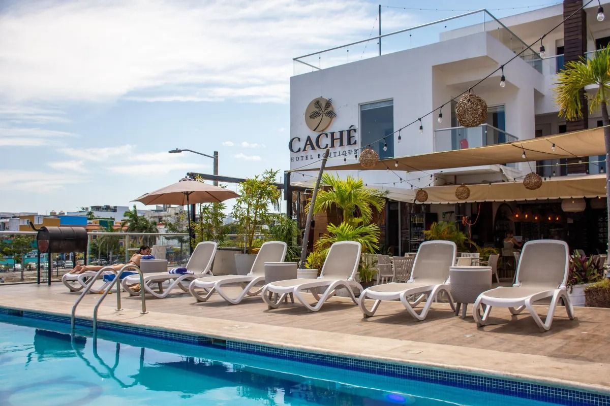 A swimming pool next to a row of lounge chairs on a deck, with a hotel building featuring a