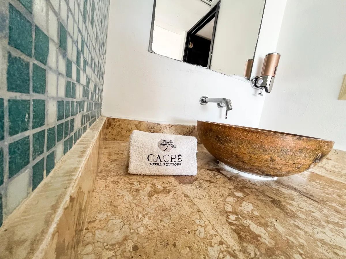 A stone sink and a branded towel on a beige marble countertop next to a blue tiled wall in a hotel bathroom.