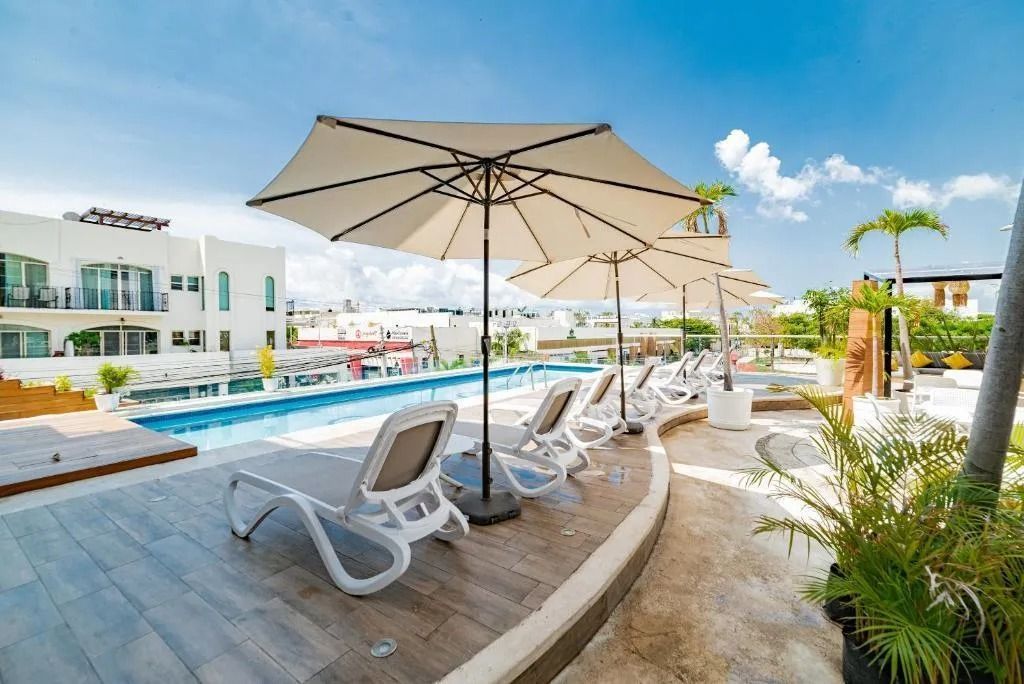 Lounge chairs and umbrellas by a rooftop pool at a resort under a blue sky.