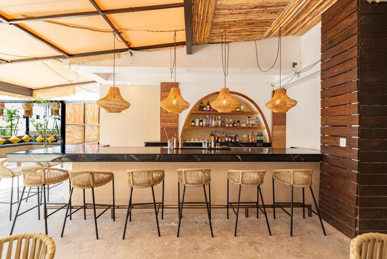 A bar with a dark marble counter and row of woven rattan bar stools under decorative hanging lamps in a rustic setting.