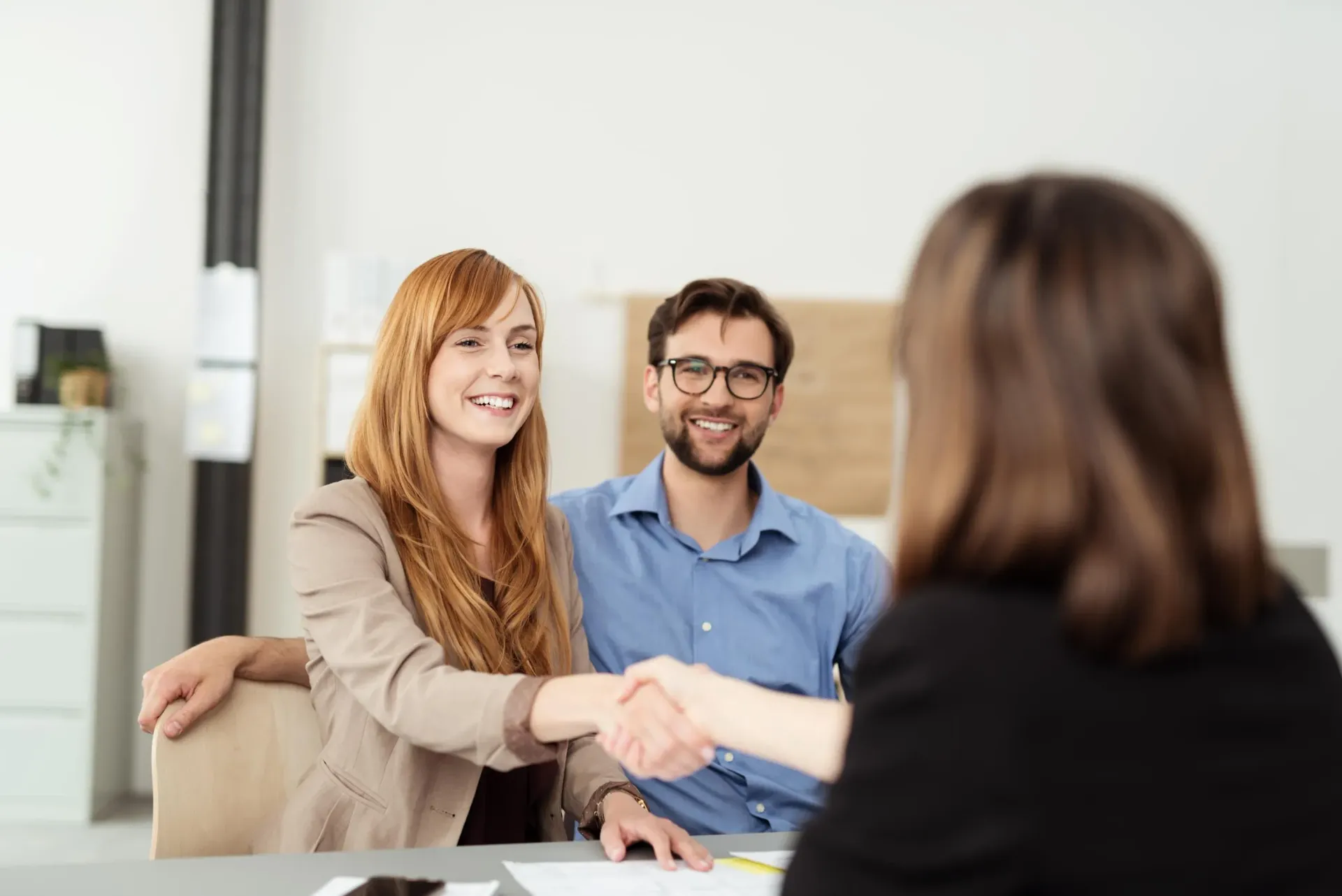 A man and a woman are shaking hands with a woman while sitting at a table.
