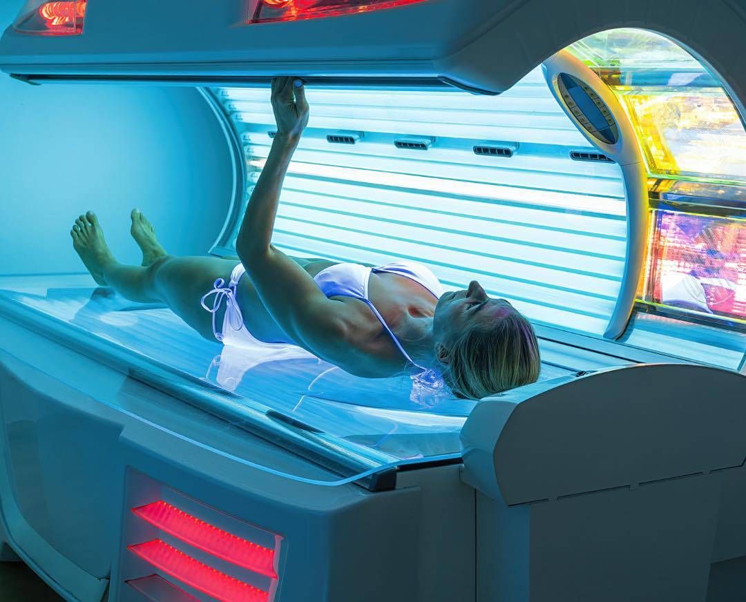 Woman lying in a tanning bed; bright blue lights, wearing a bikini.