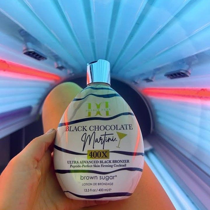 A person in a tanning bed holding a bottle of Black Chocolate Martini tanning lotion.
