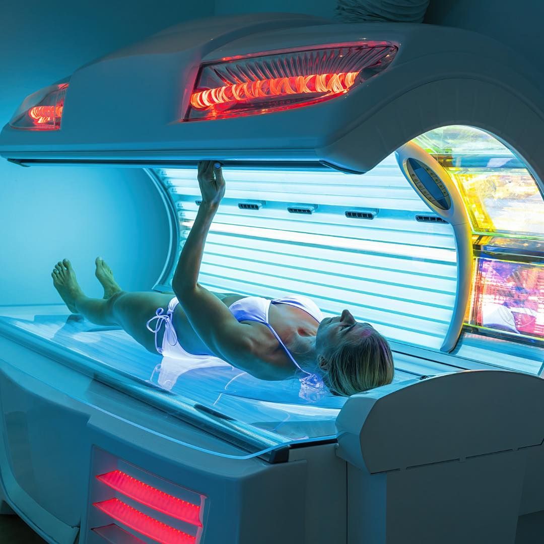 Woman tanning in a tanning bed, wearing a bikini. Blue lighting, overhead red lights.