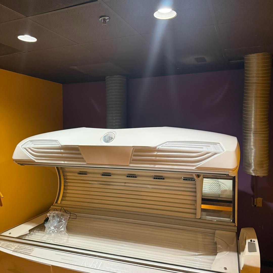 Tanning bed in a room with yellow and purple walls, ceiling lights, and ventilation tubes.