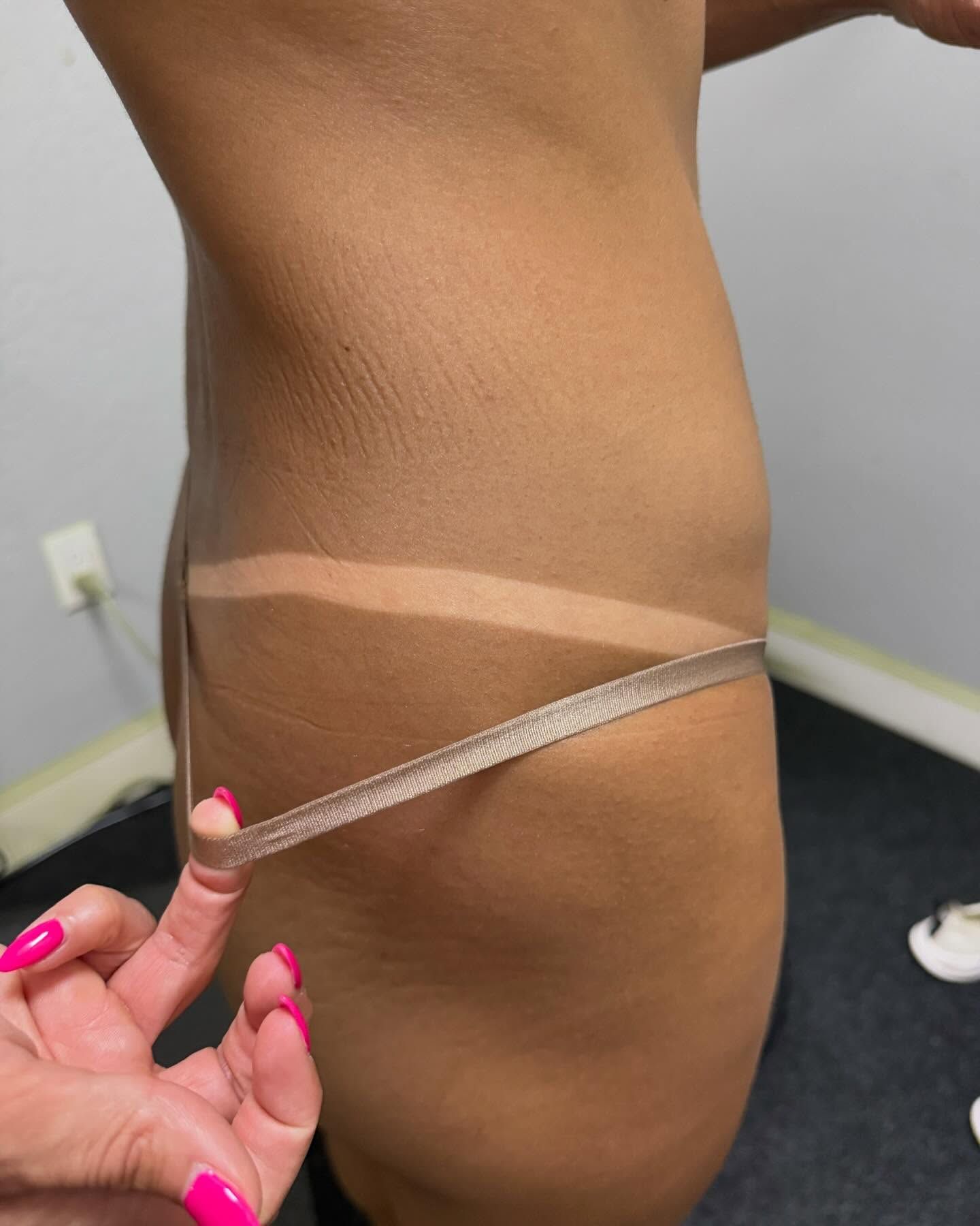 Person's side profile with a tan line, measuring tape across the waist. Pink nail polish on the hand holding the tape.