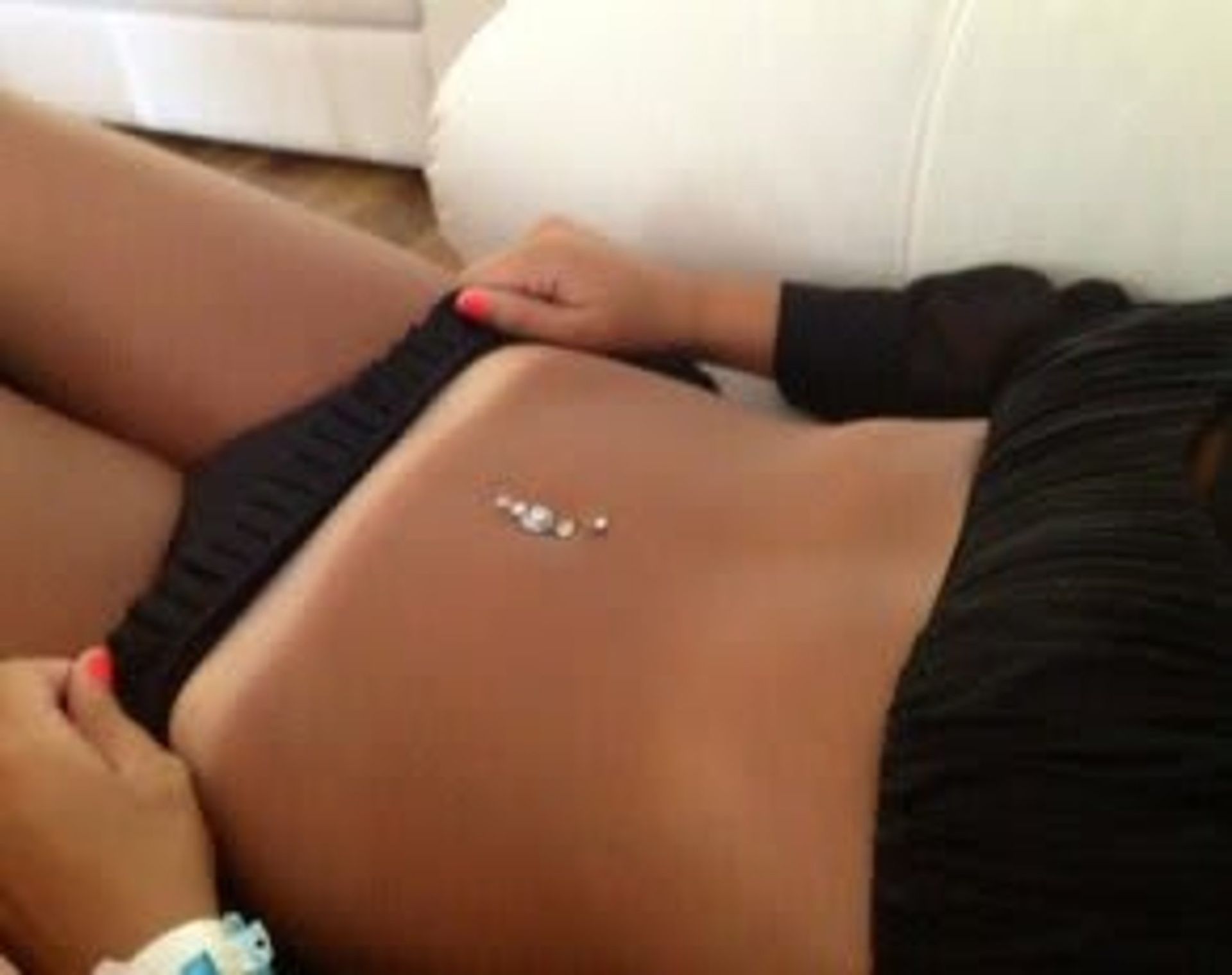 Woman with a belly button piercing wearing a black outfit, lying down.