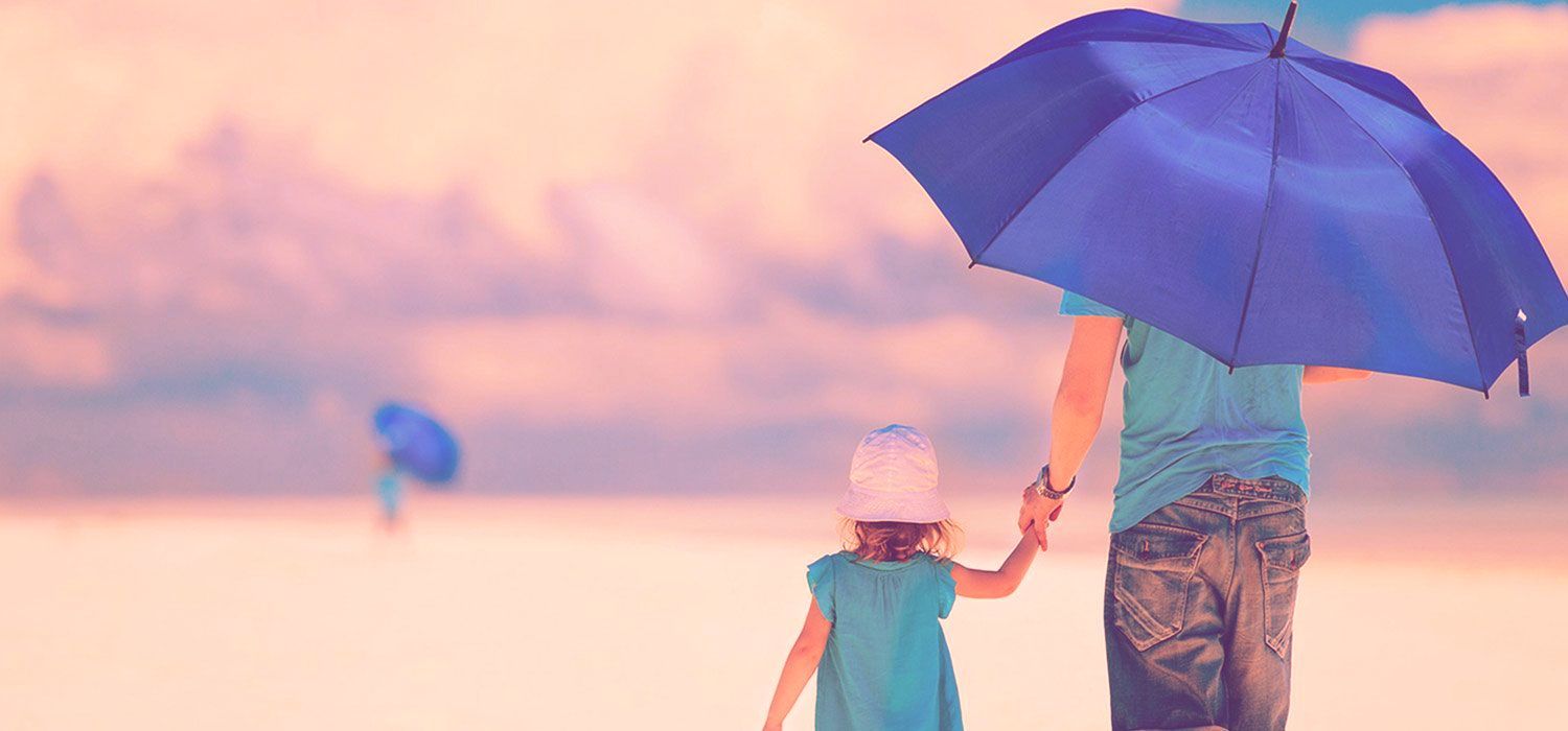 A father and child walking on a beach under a blue umbrella. Pink sky.