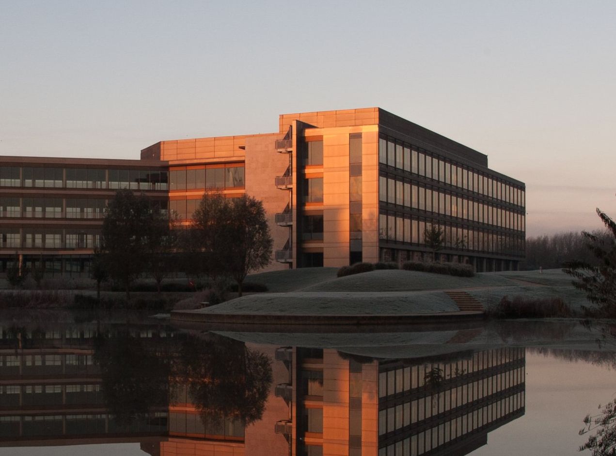 Modern building reflecting in a calm pond at sunrise, with orange and blue hues.