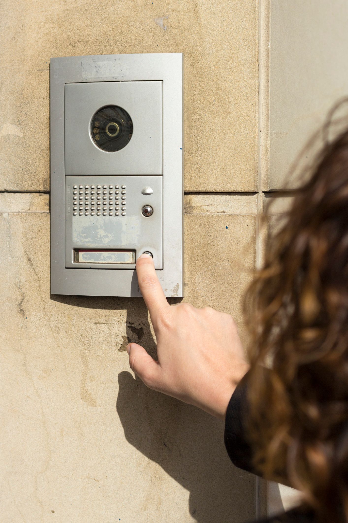 A woman uses an intercom with a camera for secure entry through commercial access control systems.