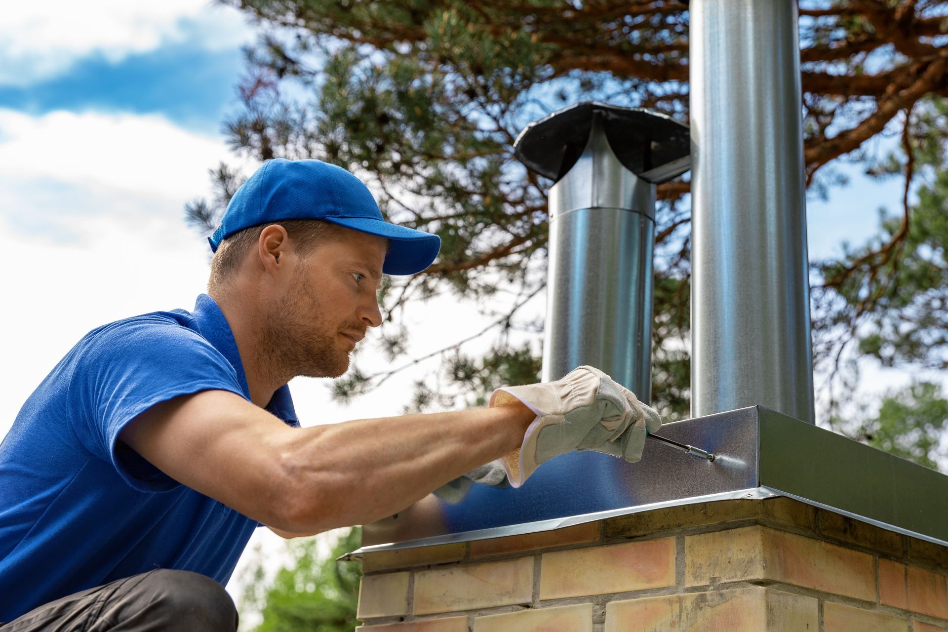 Man in blue shirt and cap working on a chimney with a metal flue.