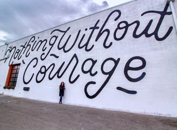 Mary Wright stands in front of mural at the Showroom: Nothing Without Courage
