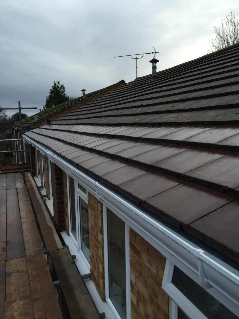 Scaffolding set up beside a brick building with a newly installed white gutter and brown tiled roof.