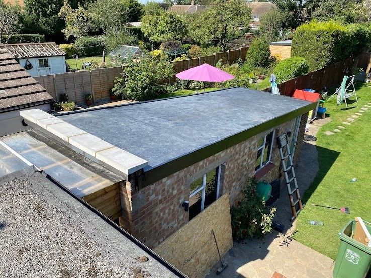 High-angle view of a flat-roofed brick garage with a dark, newly installed roof and a short stone parapet wall.