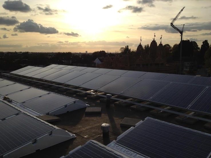 Solar panels installed in rows on a rooftop at sunset, with silhouetted temple spires visible in the distance.