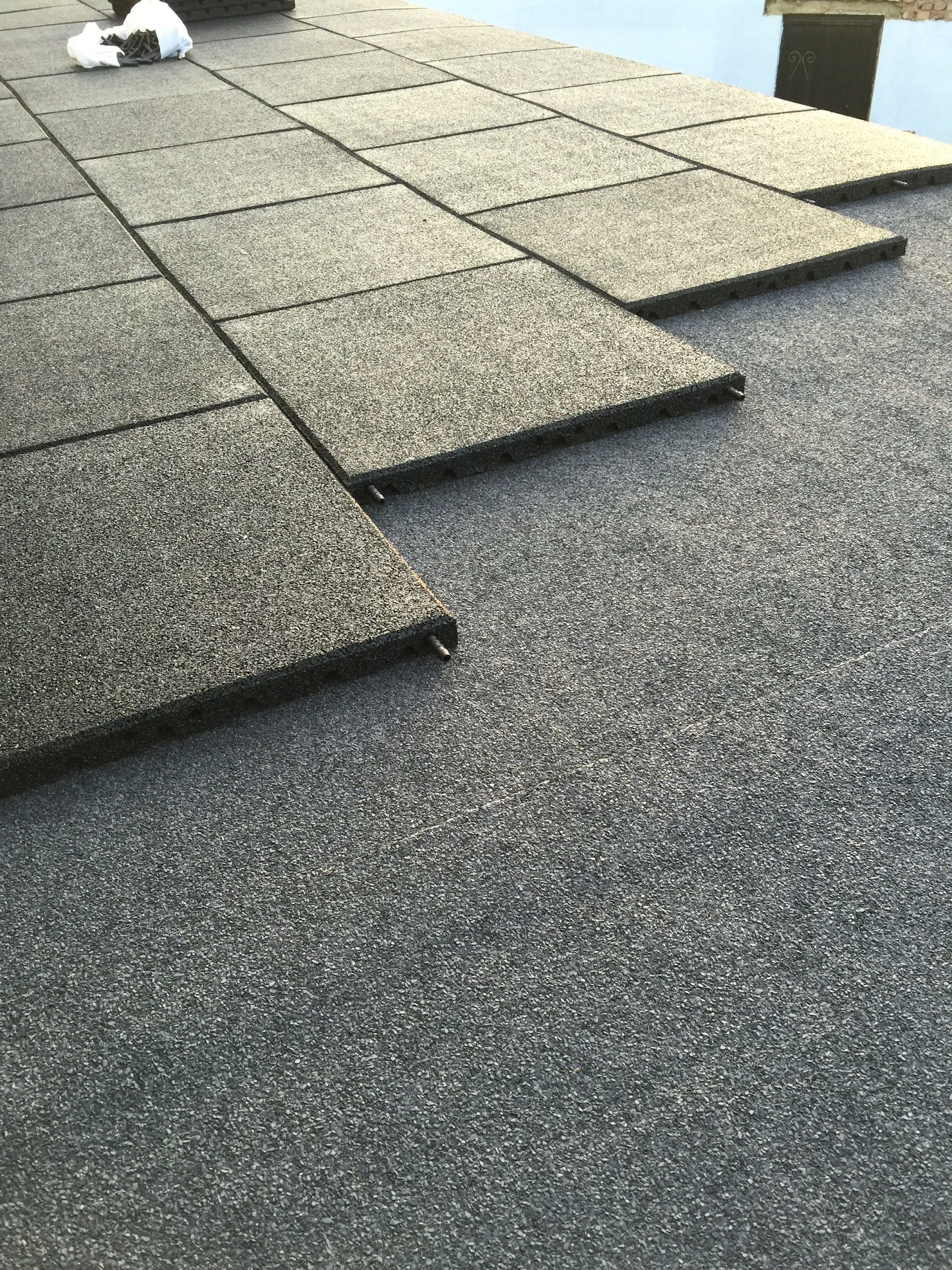Gray, square interlocking rubber flooring tiles being laid over a matching textured surface.