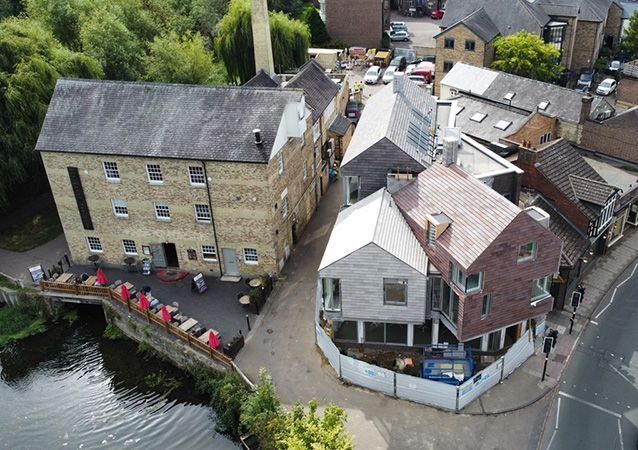 An aerial view shows an older stone mill building next to a modern construction site with new brick and metal structures.