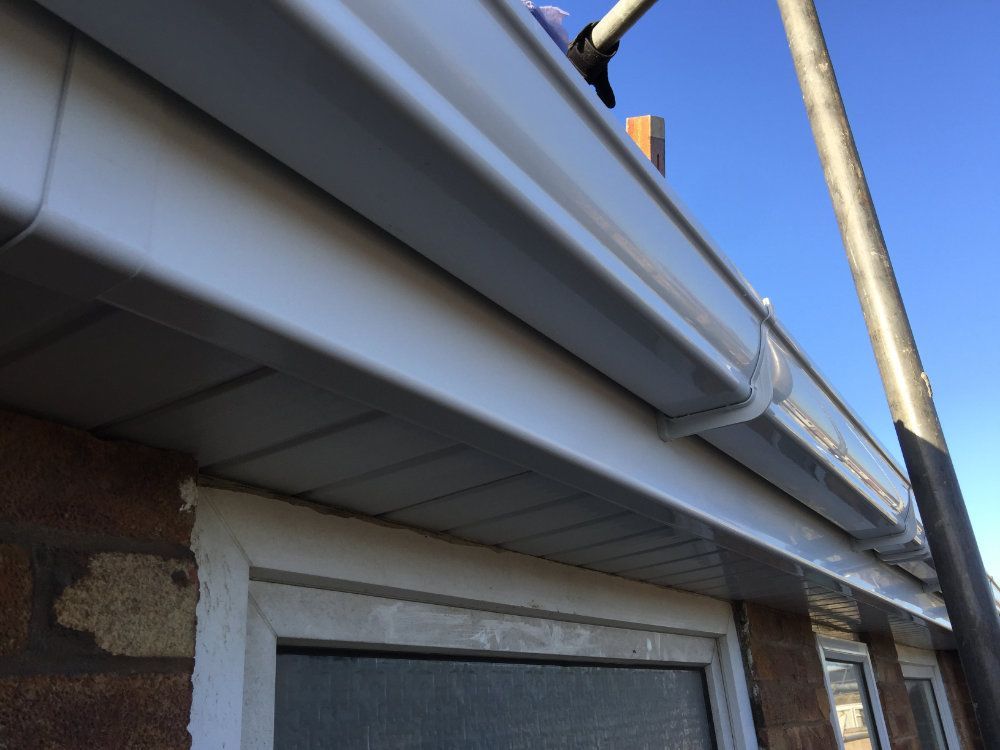 White uPVC fascia boards and a matching guttering system installed above a window against a brick exterior wall.