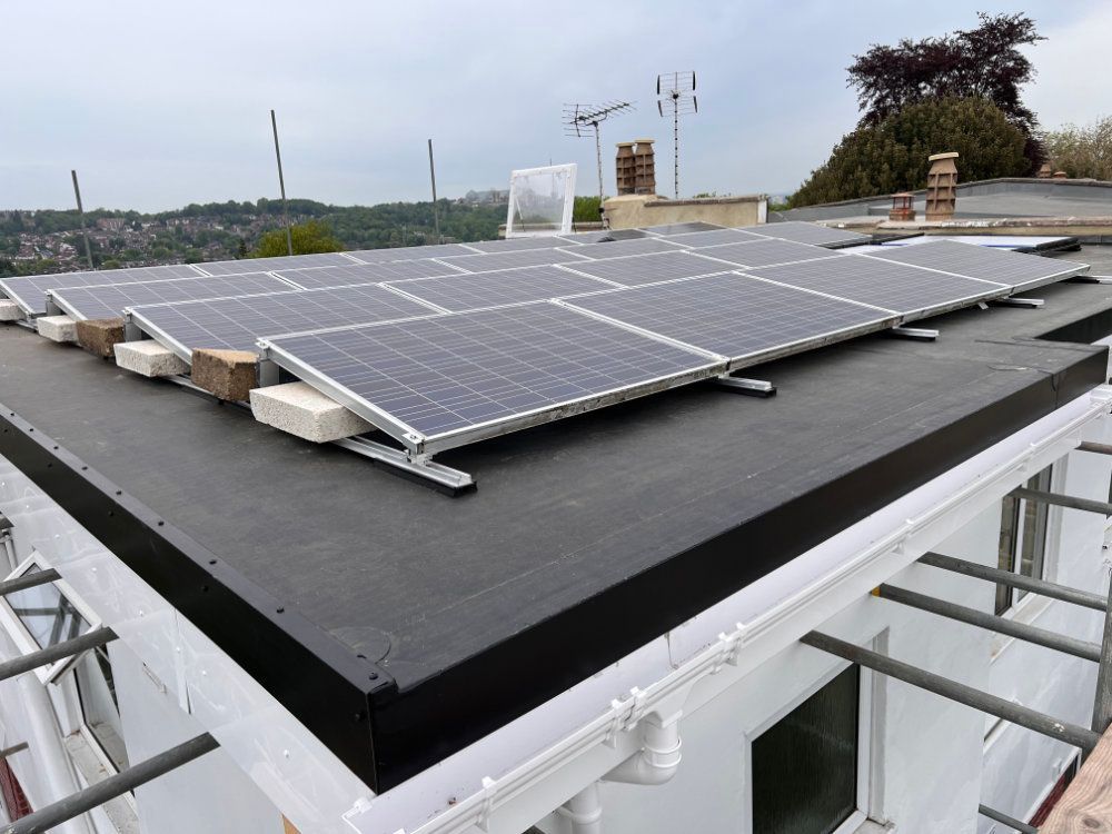 Solar panels installed on a flat, black roof of a white building, secured with bricks at the base.