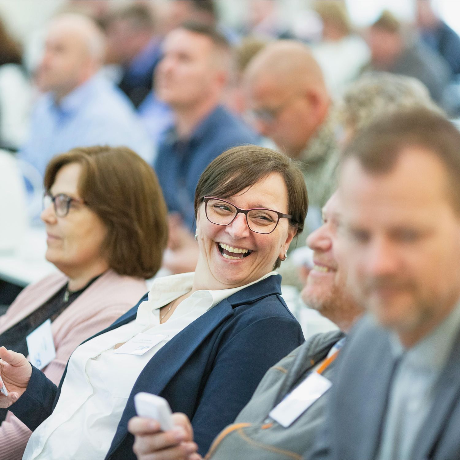 A woman is smiling while sitting in a crowd of people.