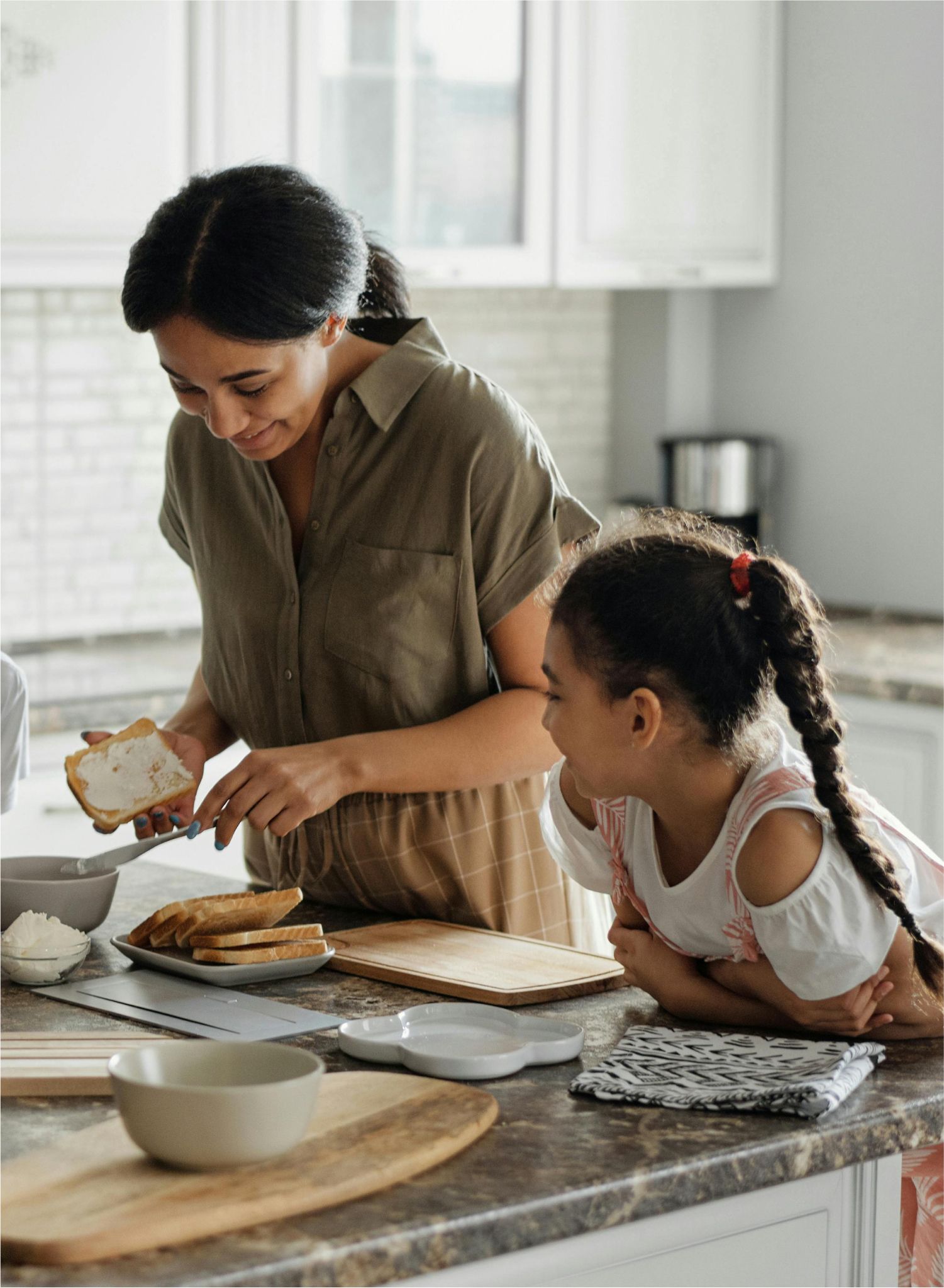 A woman and a little girl are preparing food in a kitchen.