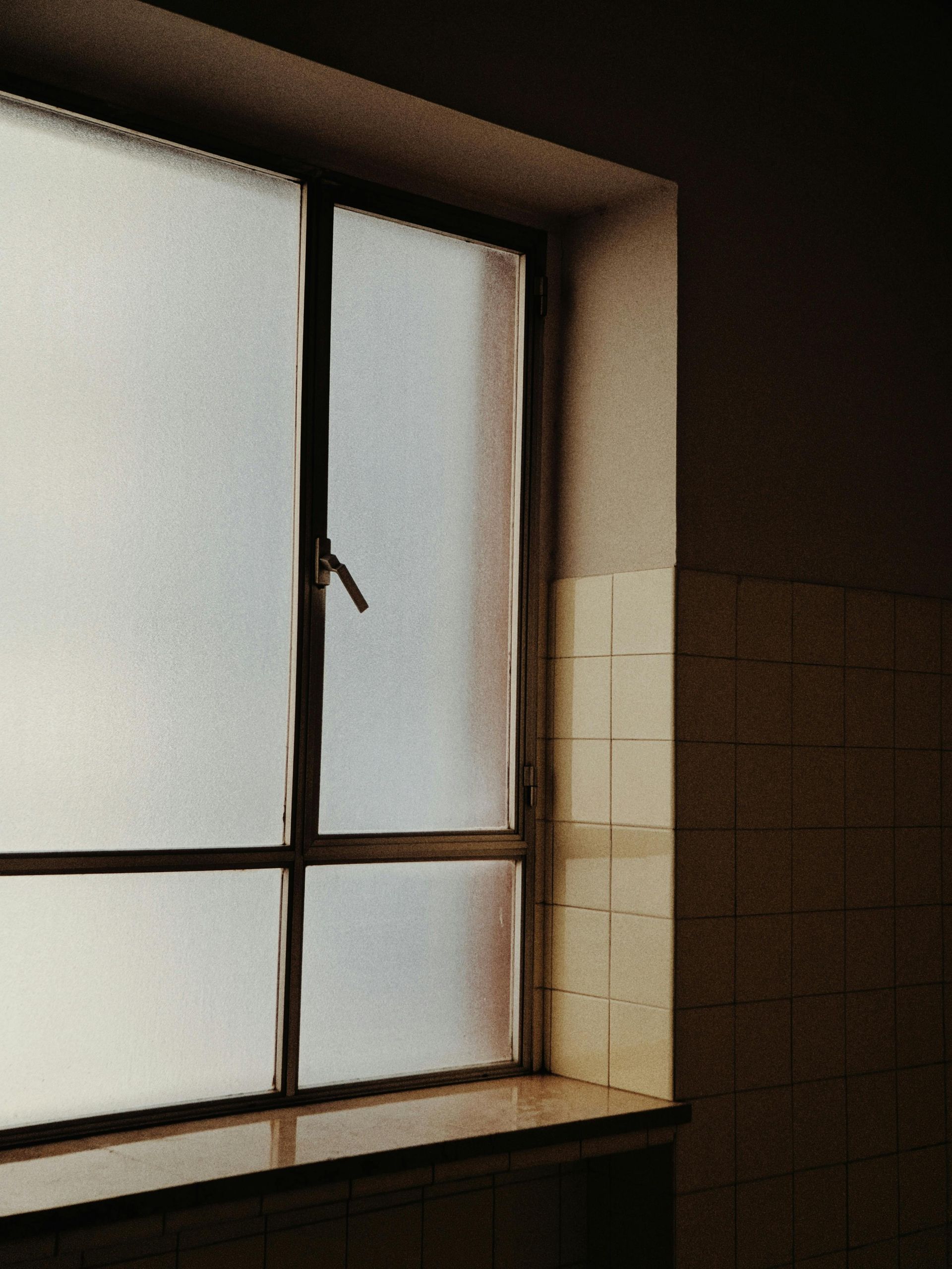 A window in a dark room with a tiled wall