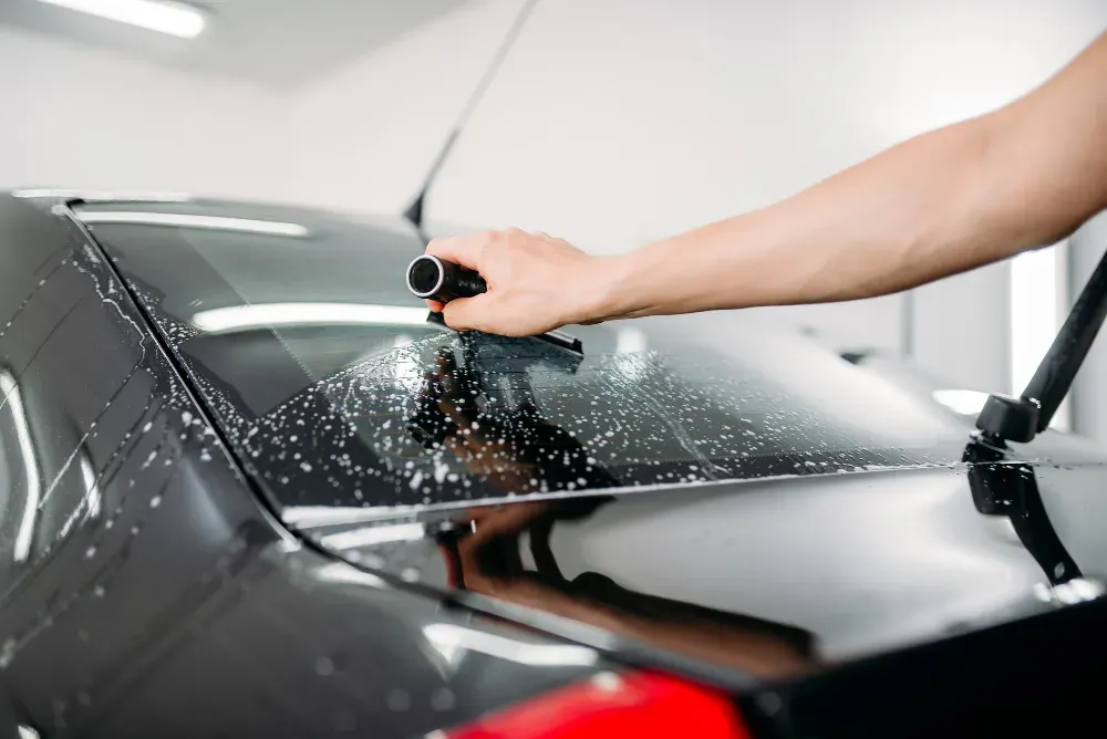 Mobile Window Tint - A man is spraying a car windshield with a spray bottle.