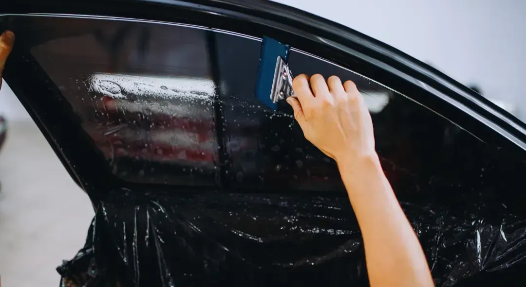 A woman is applying tinted window film to a car window.