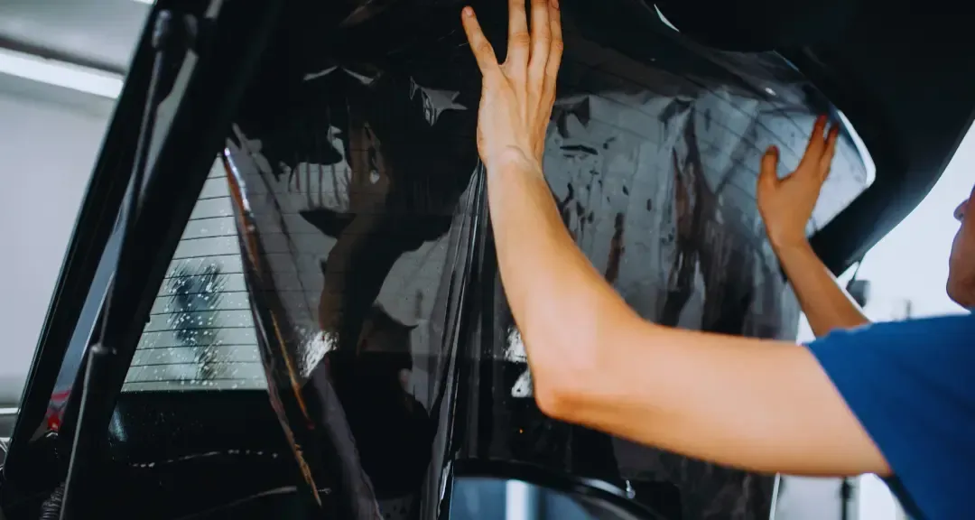 A person is applying tinted glass to a car window.