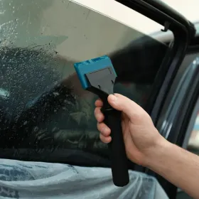 A hand holding a window tinting tool  using it in a car window