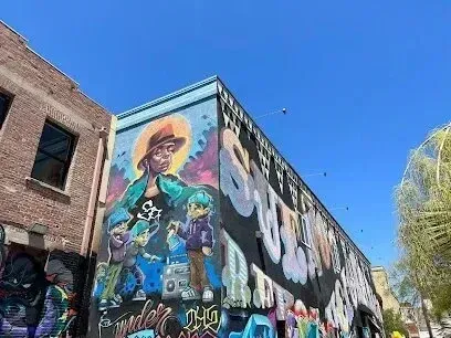 Window Tinting Service-Mural on a building of a person with two children; graffiti on the lower sections against a blue sky.