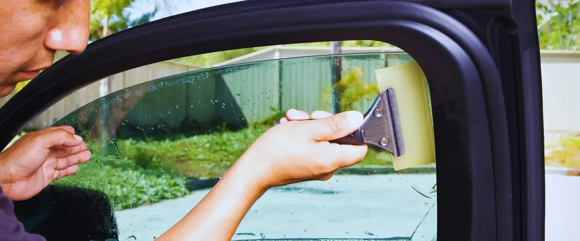 A man is applying tinted window film to a car window.