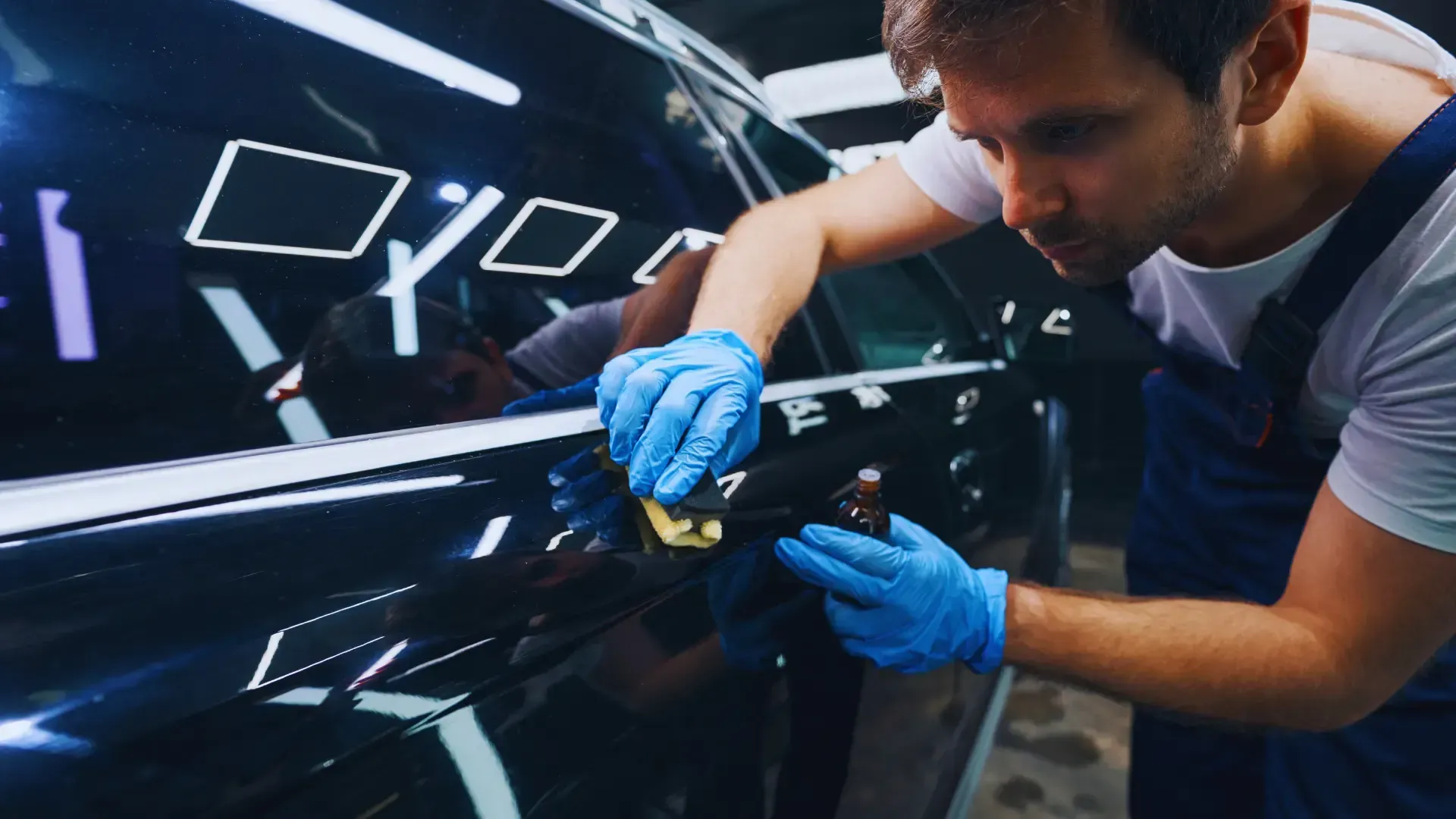 A man wearing blue gloves is polishing a car in a garage.