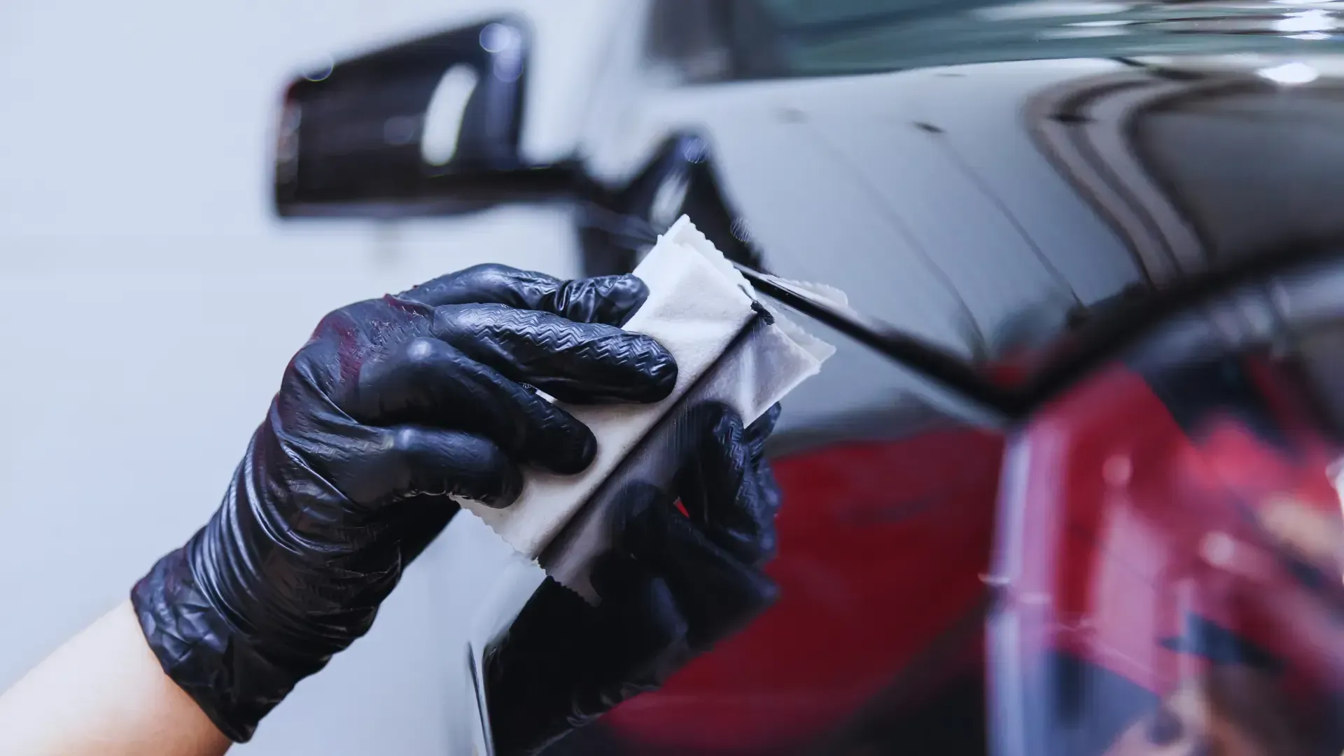 A person wearing black gloves is polishing the hood of a car.