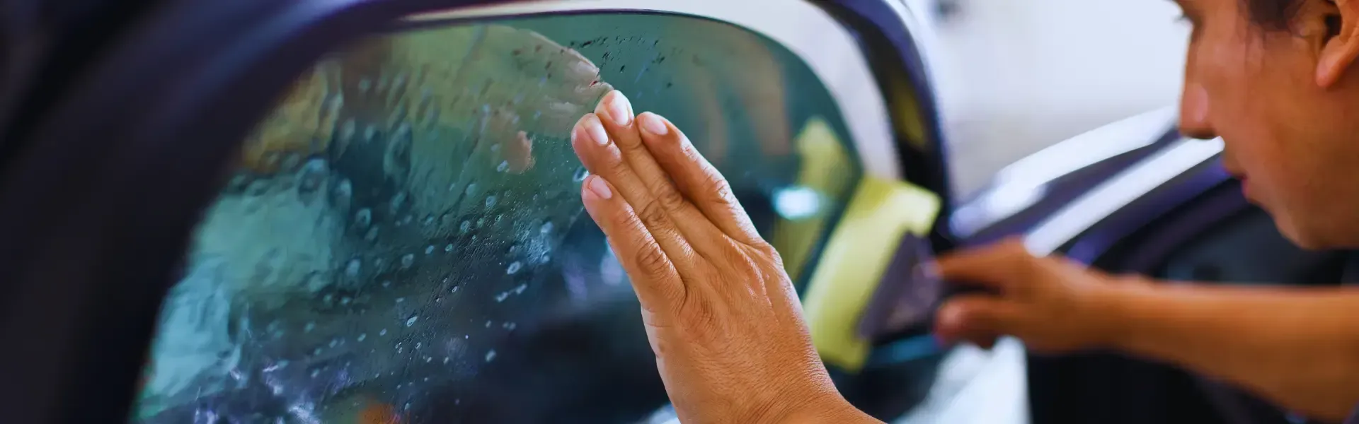 A person is applying tinted window film to a car window.