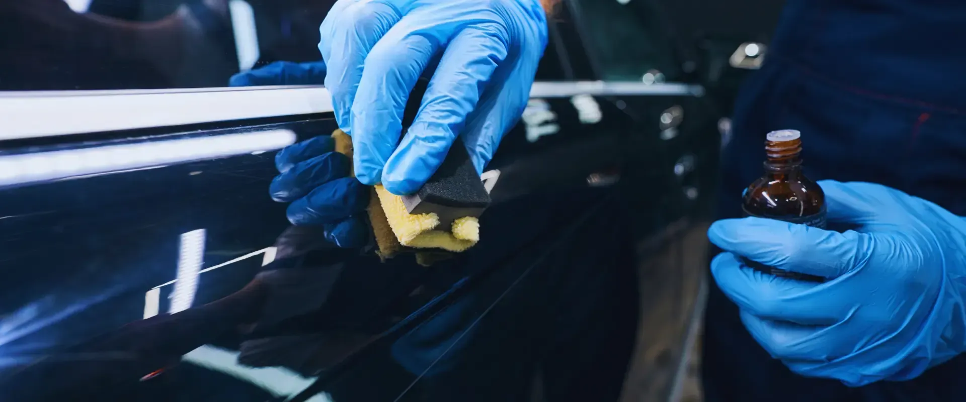 A person wearing blue gloves is polishing a car with a sponge.