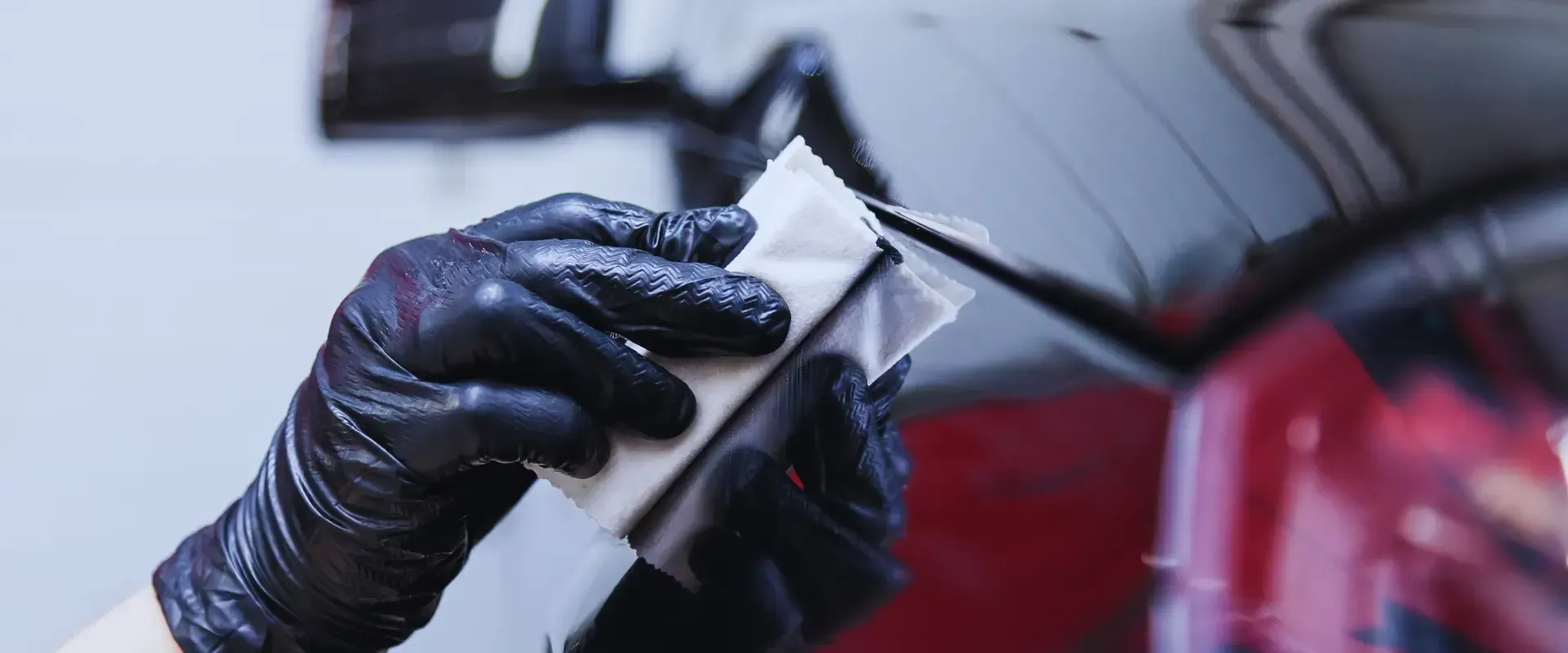 A person wearing black gloves is cleaning a car with a cloth.