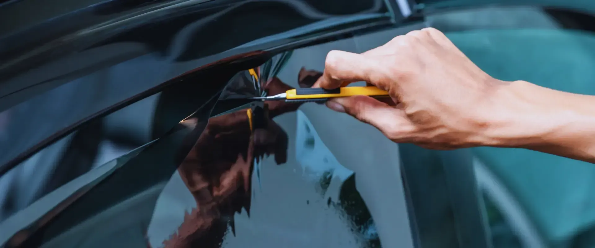 A person is installing a window tint on a car with a screwdriver.