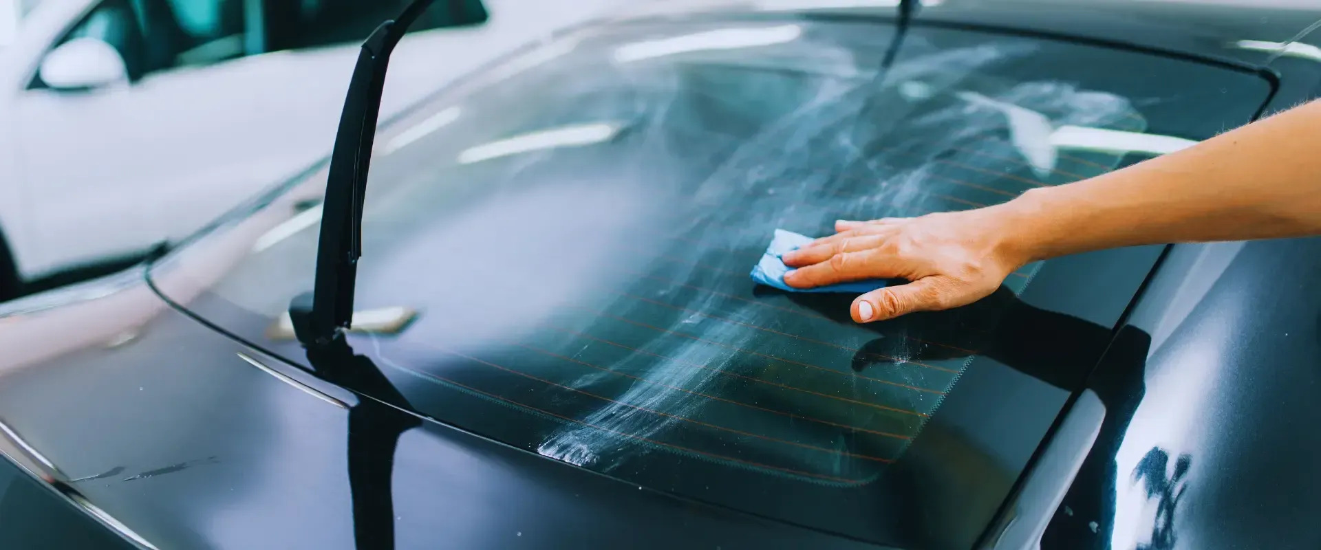 A person is cleaning the windshield of a car with a cloth.