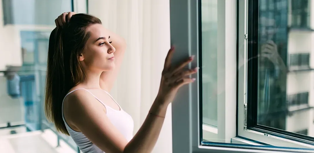 A woman is standing in front of a window looking out.