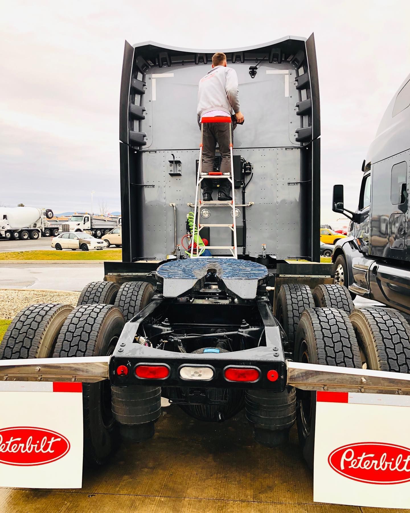 A man is standing on a ladder on the back of a peterbilt semi truck.