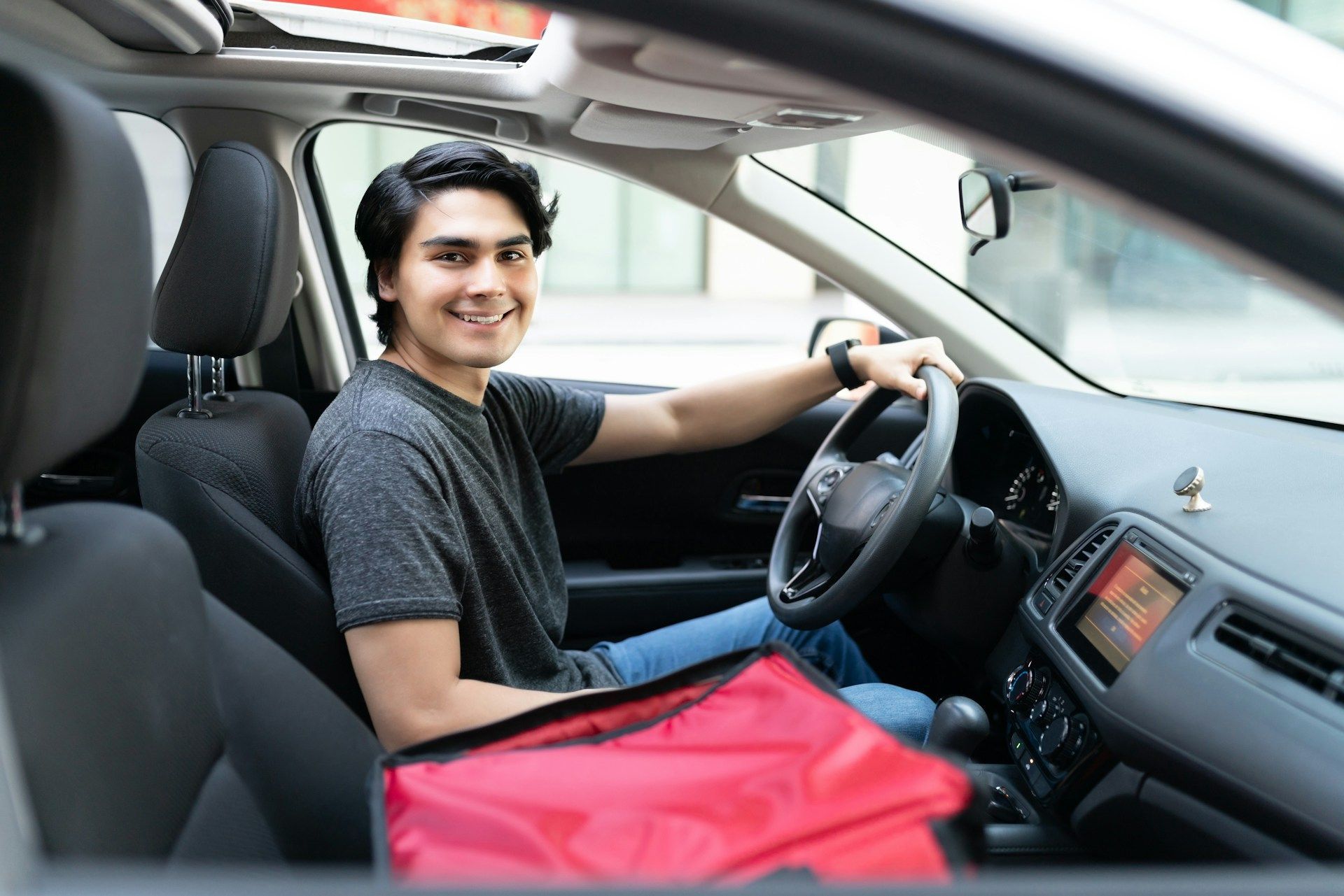 Smiling driver sitting in a car with a red bag on the passenger seat