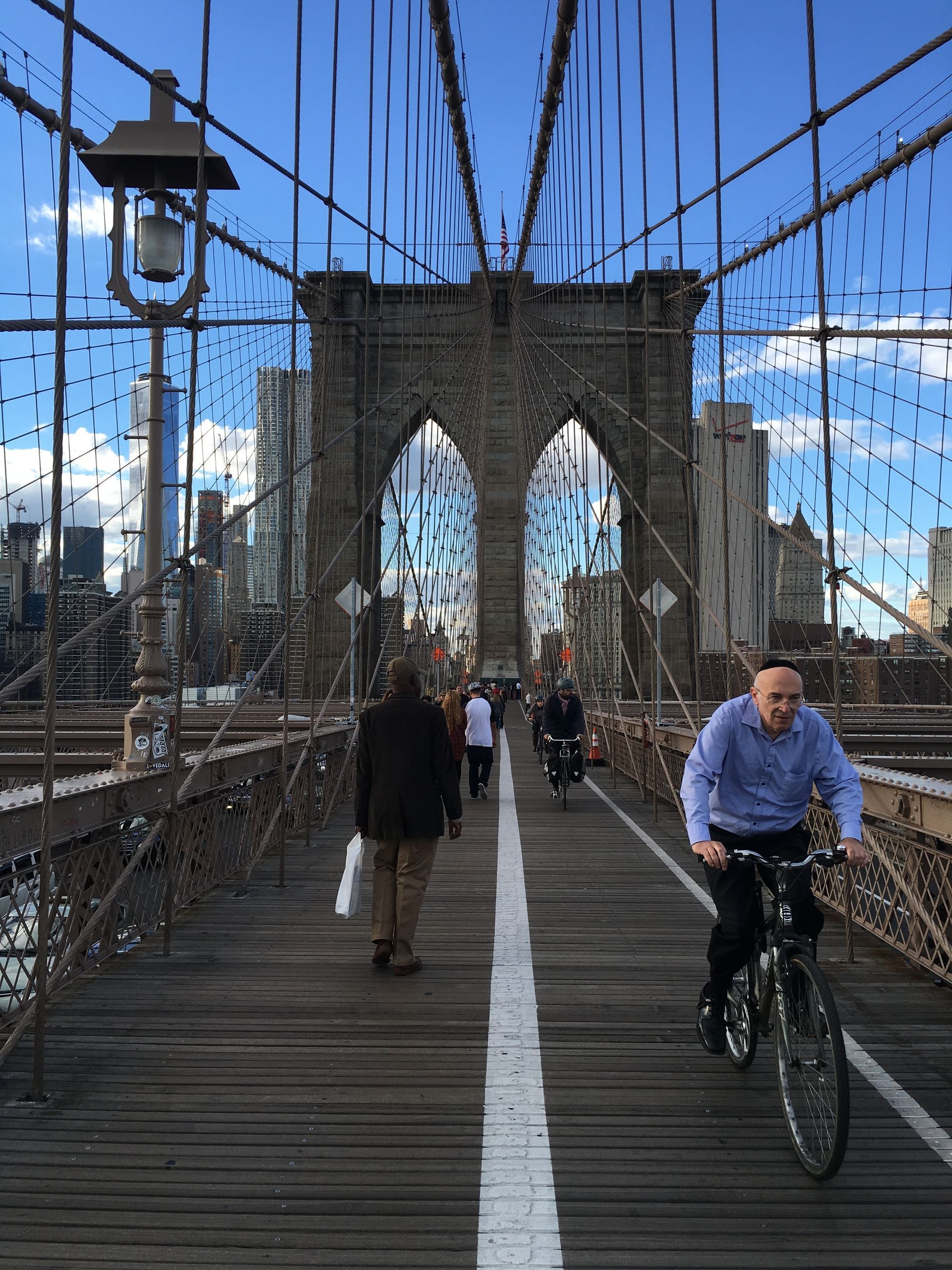 Pedestrians and a cyclist on the Brooklyn Bridge walkway under a bright blue sky