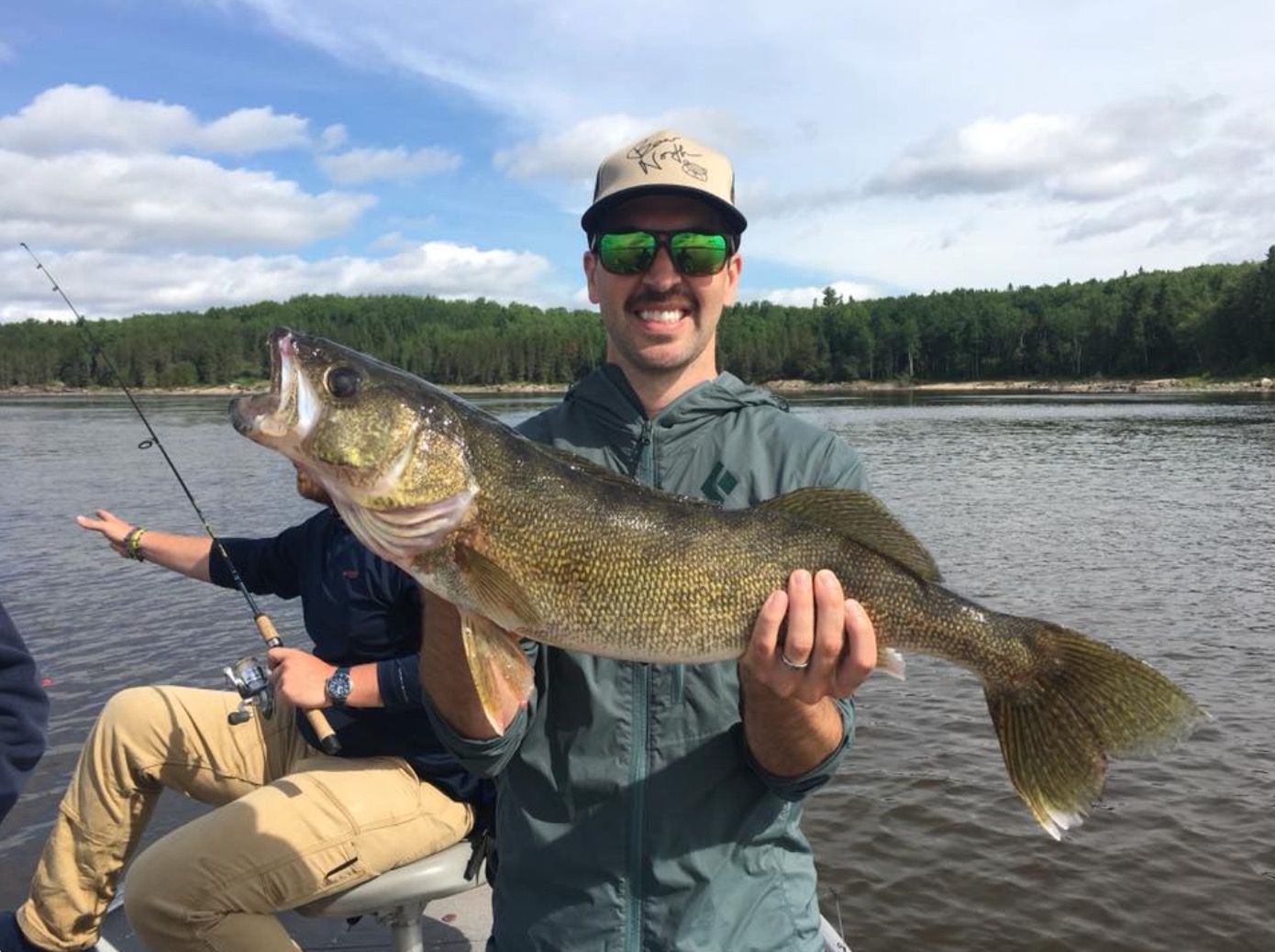 Man in green jacket holding up walleye on a summer's day.