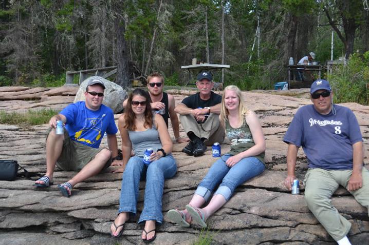 A family sitting on the Canadian Shield enjoying a  fish fry of walleye for a shore lunch at Oak Lake Lodge.